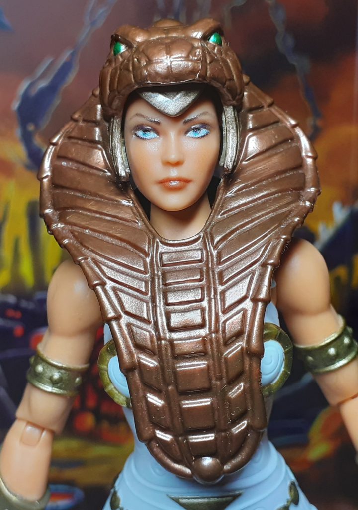 In this photo, the New Eternia Teela figure has the snake themed armour on. This is moulded in a shiny metallic bronze colour and covers the figure's head and torso.