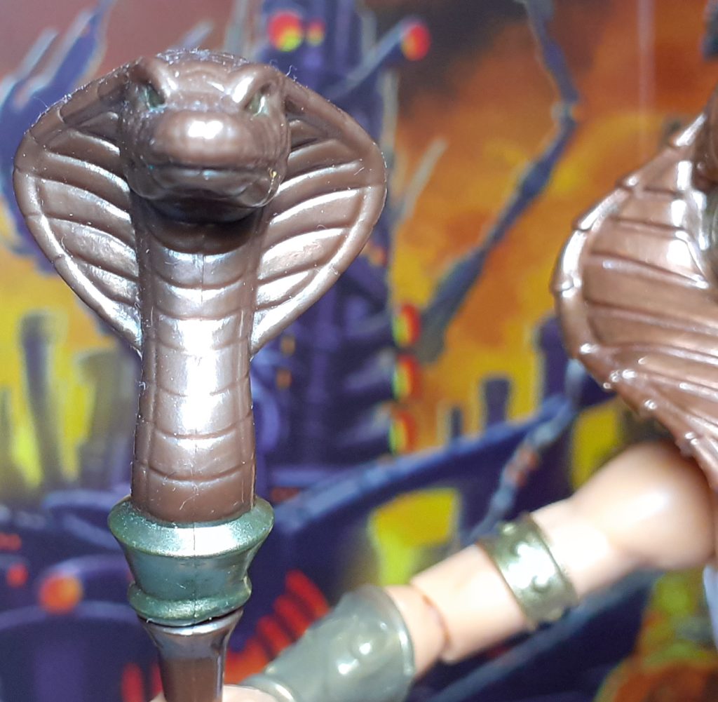 A close up photo of the snake head of New Eternia Teela's staff. This is moulded to look like a cobra's head with its hood flaring out to the sides.