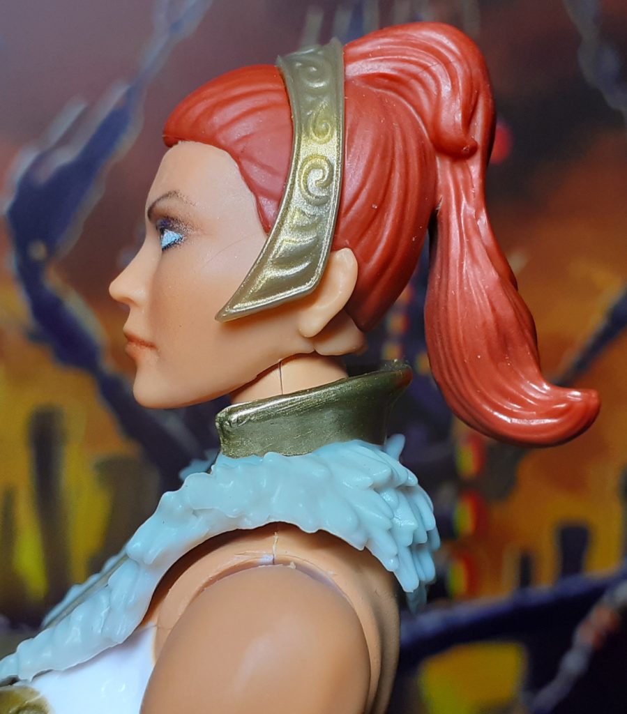 The side of the head for New Eternia Teela. The red hair goes up and behind the gold tiara and hangs in a pony tail on the back of the head.