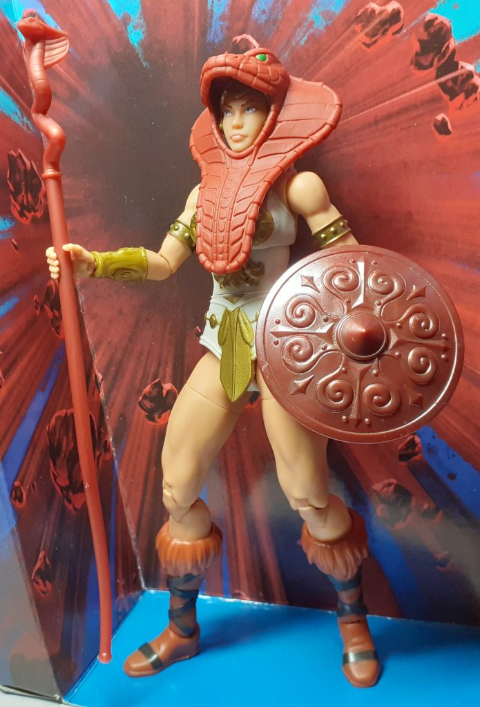 A photo of the action figure Vintage Collection Teela. The figure is slightly off centre and looking off to the left of the viewer. It's wearing the cobra snake armour and is holding the cobra headed staff in the right hand and the shield in the left hand.