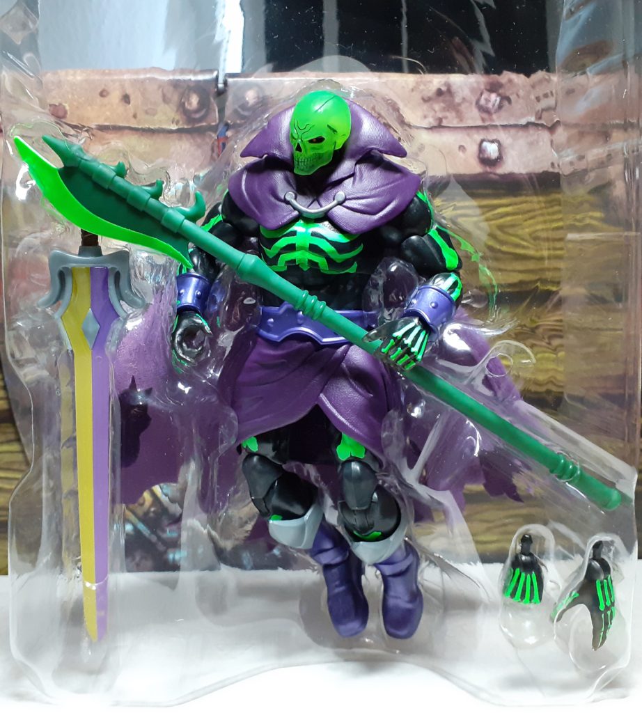 In this photo, the Scare Glow figure has been removed from the display box but is still in the clear plastic packaging. The figure and its accessories are clear to see - the halberd is held across the figure, to the left of the photo is the Sword of Power and in the bottom right is the extra pair of hands.