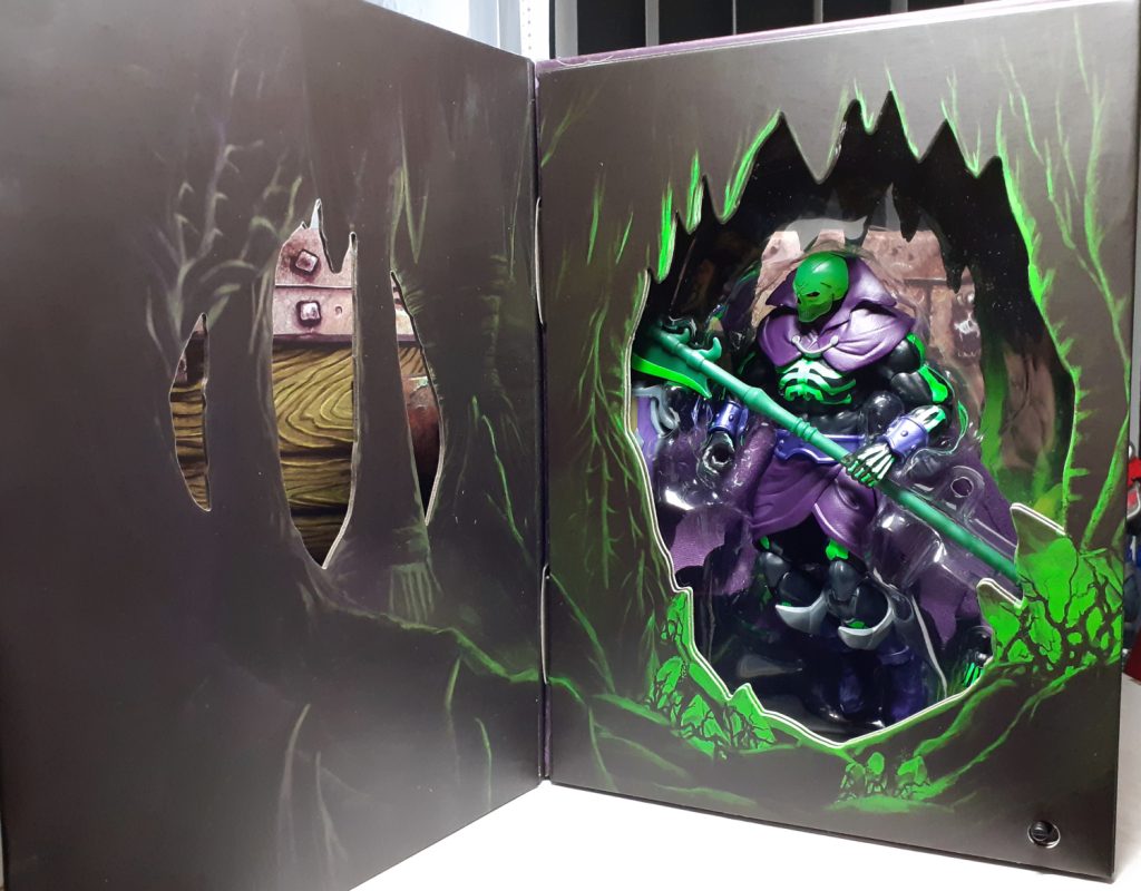 The front of the display box with the cover opened. More of the cave design can now be seen with stalagmites and stalactites with glowing green edges visible. Through the cave opening more of the Scare Glow figure can be seen.