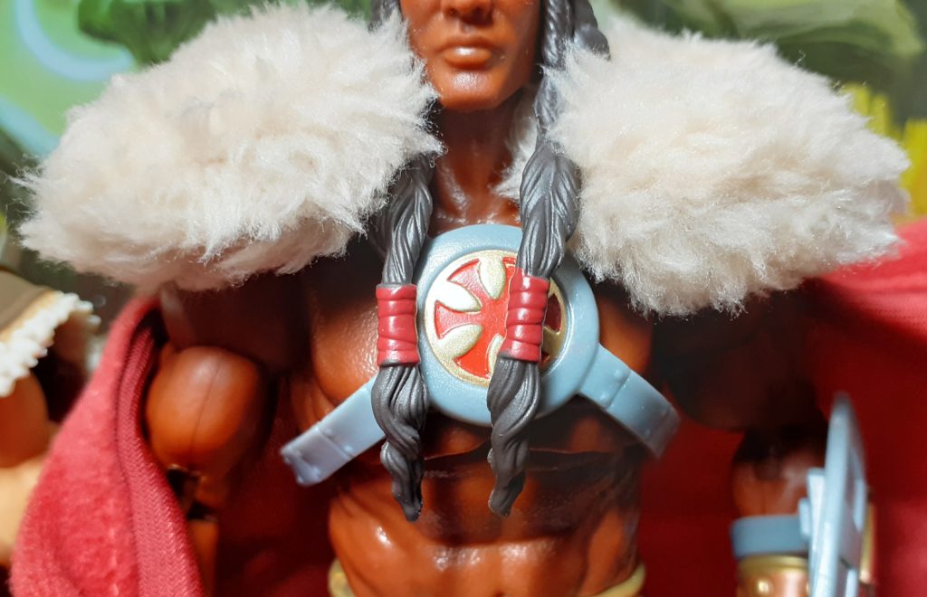 The front of Revelation King Grayskull's chest harness. This also has an "asterisk" cross design in red on a gold background. The rest of the harness is a moulded grey plastic.