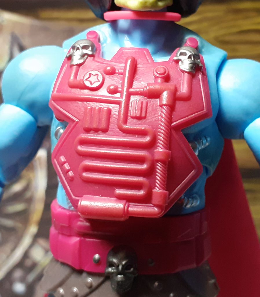 The large, magenta coloured chest plate on the front of the torso of the Skeletor figure. It features some raised details that look like tubes and two silver skulls at each of the top two corners.