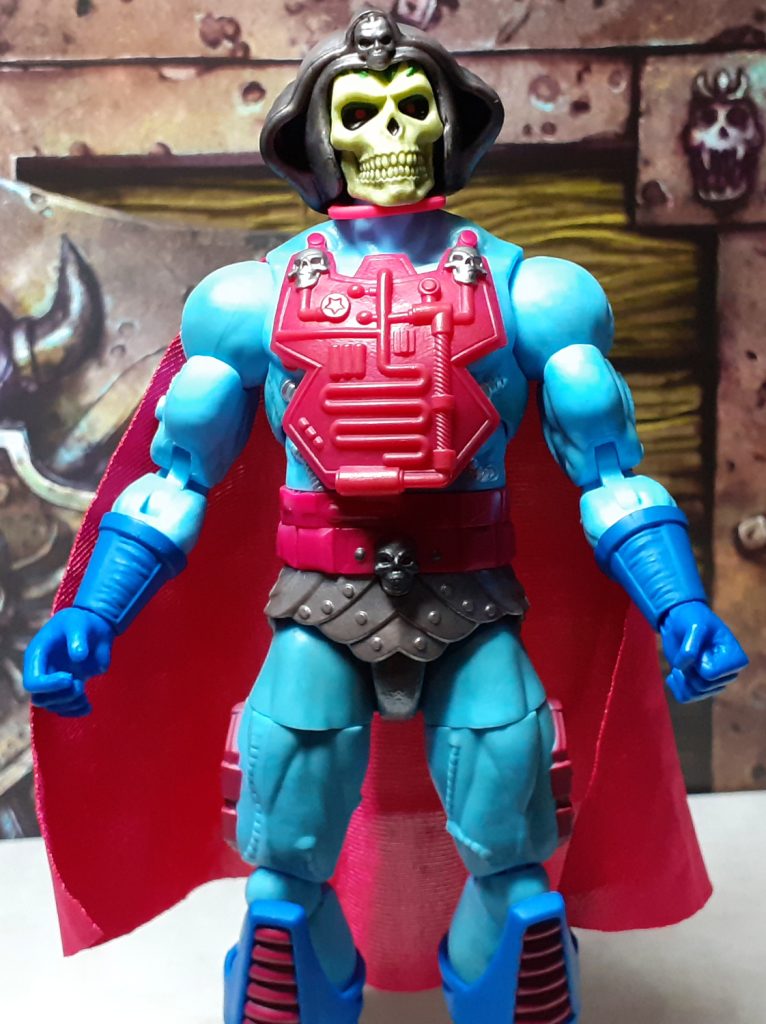 The Skeletor figure standing straight with its arms down by its sides. The pinky magenta cape is spread out over the back of the figure and extends down to knees. It's attached to the figure by a large choker over the neck.