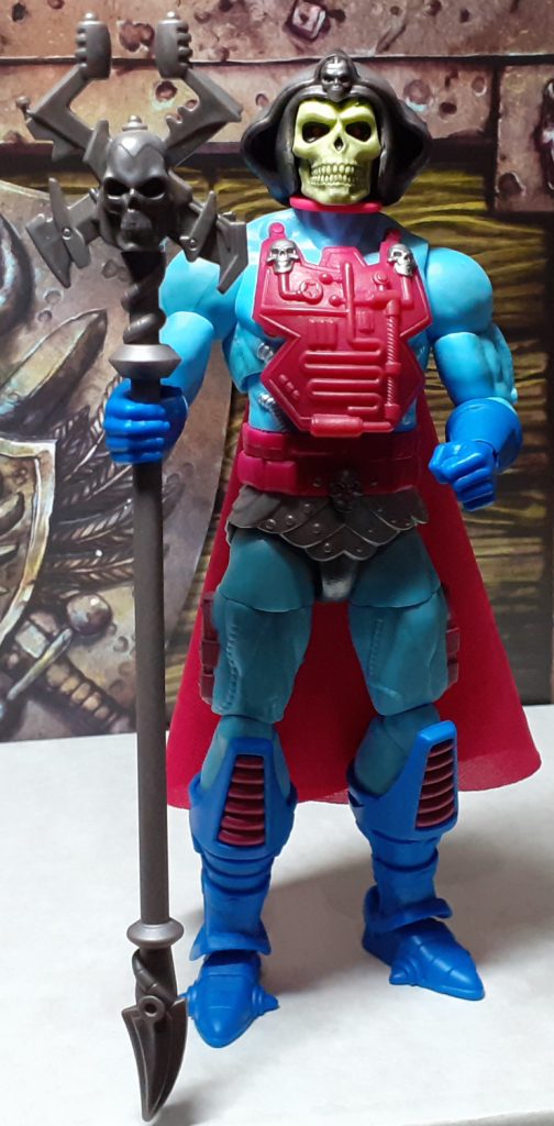 The Skeletor figure standing straight and holding the Havoc Staff in its right hand. The staff is a gun metal grey plastic and is roughly as tall as the figure. At the top of the staff is a human skull design with four metal blades coming out from it.