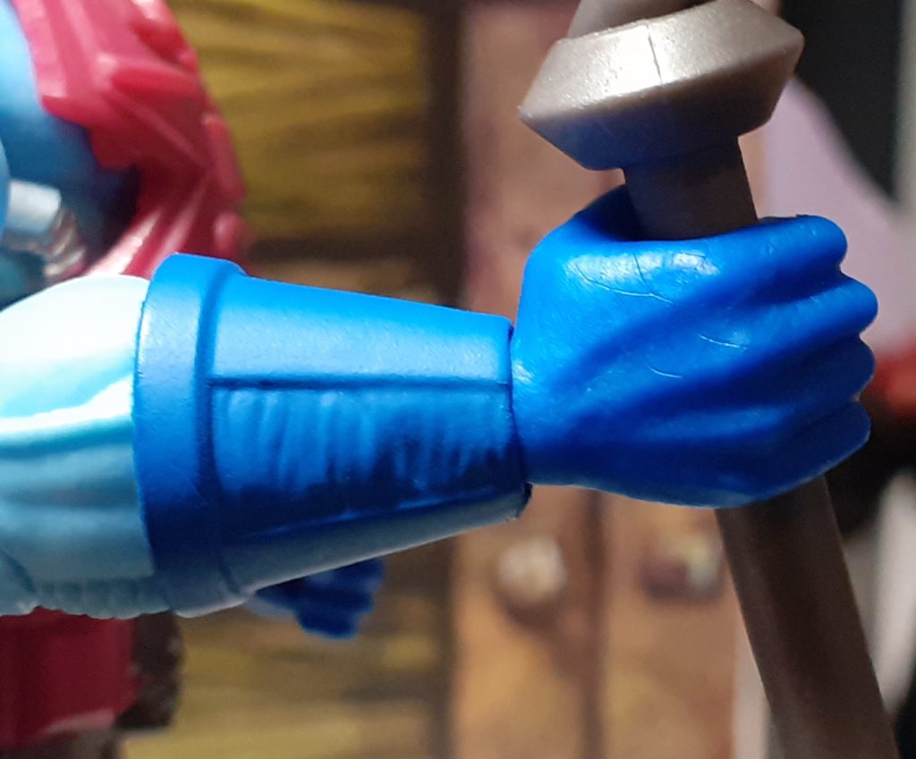 A close up photo of the right hand gripping the Havoc Staff. The hand and wrist are coloured the same mid-blue. The wrist itself has a joint that allows and up and down motion, shown here by the hand being slightly bent upwards.