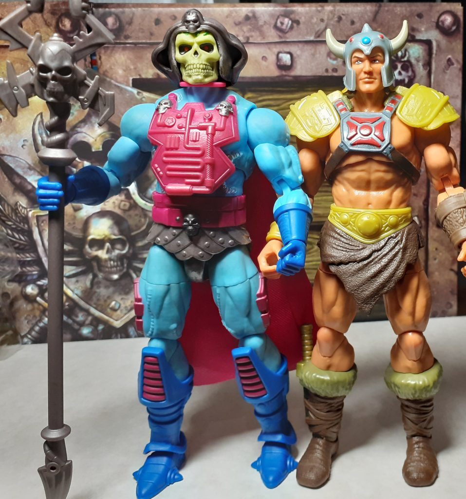 A photo comparing the heights of the New Adventures Skeletor and Viking He-Man figures. Skeletor is on the left, holding a staff in its right hand. Standing alongside on the right is the Viking He-Man figure with gold shoulder armour and a Viking style helmet complete with a pair of horns.