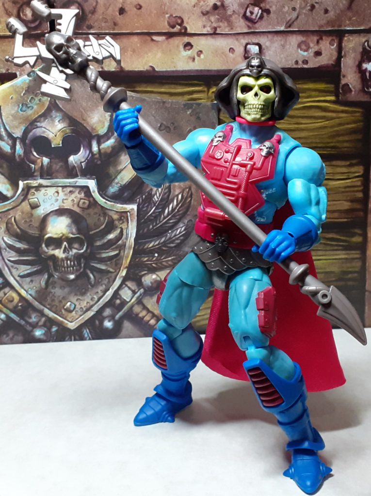 A photo of the Skeletor figure wielding the Havoc Staff. The figure is holding the staff diagonally across its body with the top to the left of the photo. The bottom of the staff is down to the right of the photo and ends in a curved blade.