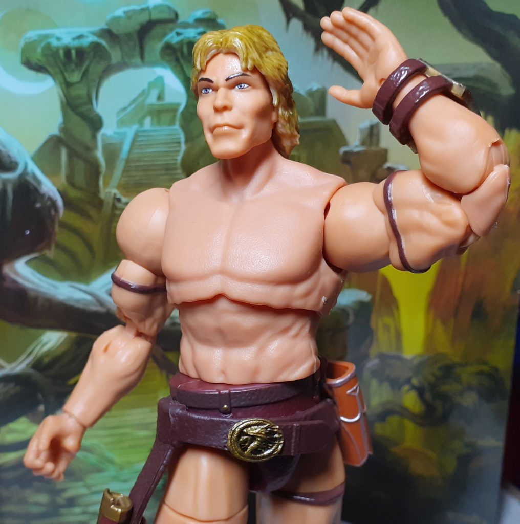 The 1987 Movie He-Man with the armour taken off so it has a bare torso. The upper part of the figure is twisted towards the left of the photo at the waist. The left arm is raised and bent at the elbow making the figure look almost as though it is doing a dance move.