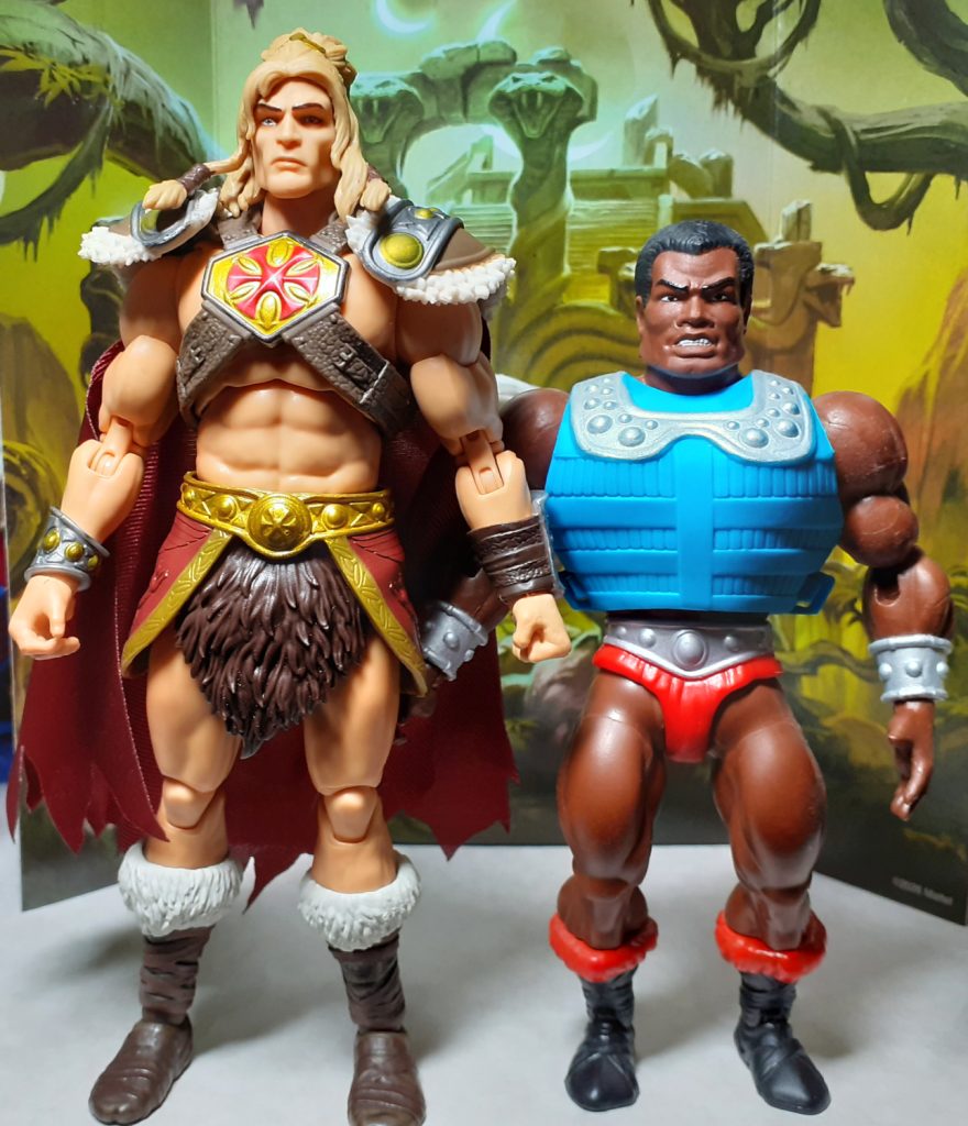 A side by side height comparison photo of the King Grayskull and Origins Clamp Champ figures. On the left of the photo is King Grayskull while on the right is Clamp Champ. Clamp Champ is wearing bright blue torso armour with a metallic silver details around the shoulders.