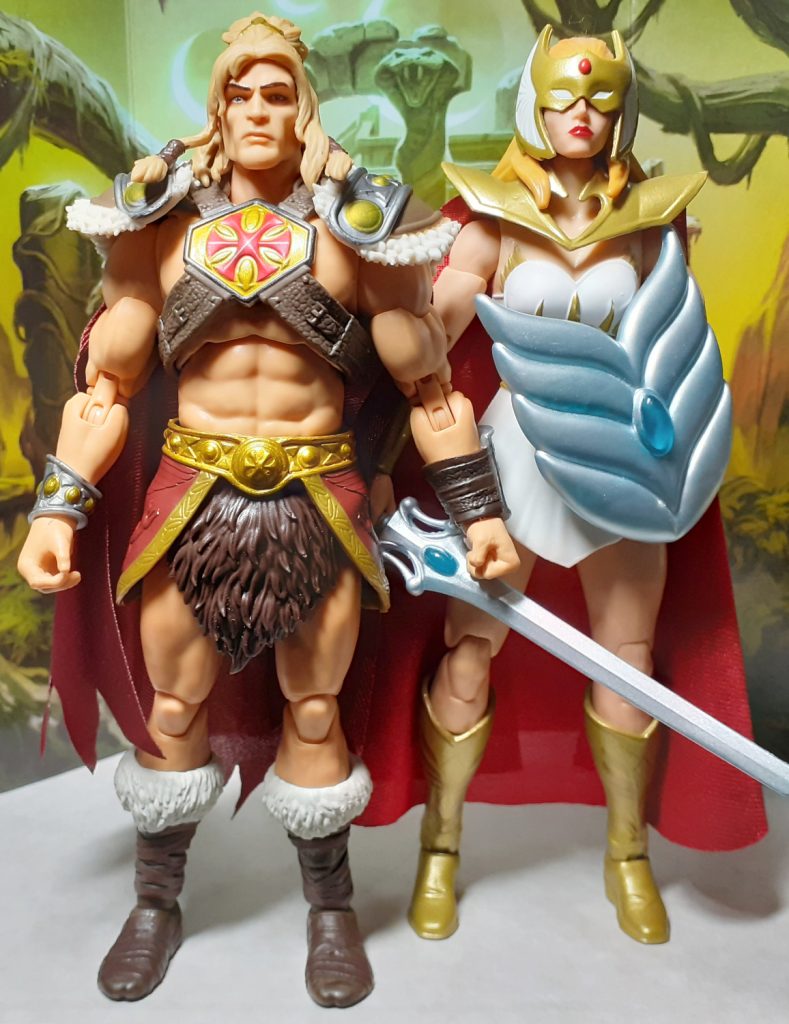A side by side height comparison photo of the King Grayskull and Princess of Power She-Ra figures. On the left of the photo is King Grayskull while on the right is She-Ra. This version of She-Ra has a golden mask over her eyes and a long red cape.